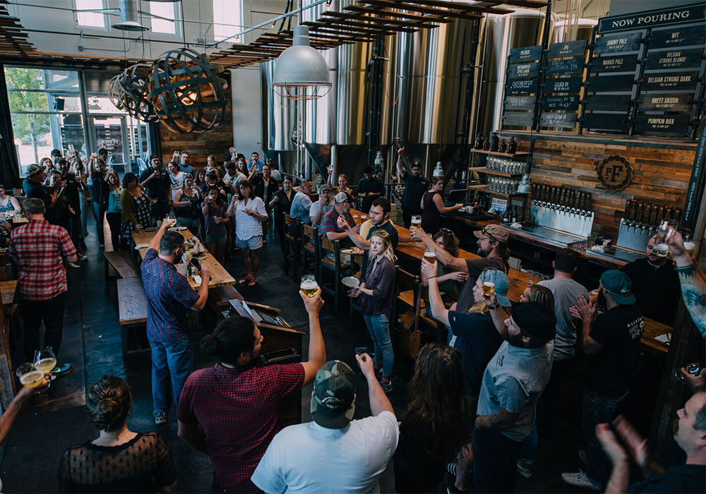 A timber-lined taproom with a long bar, warm pendant lights, and communal tables